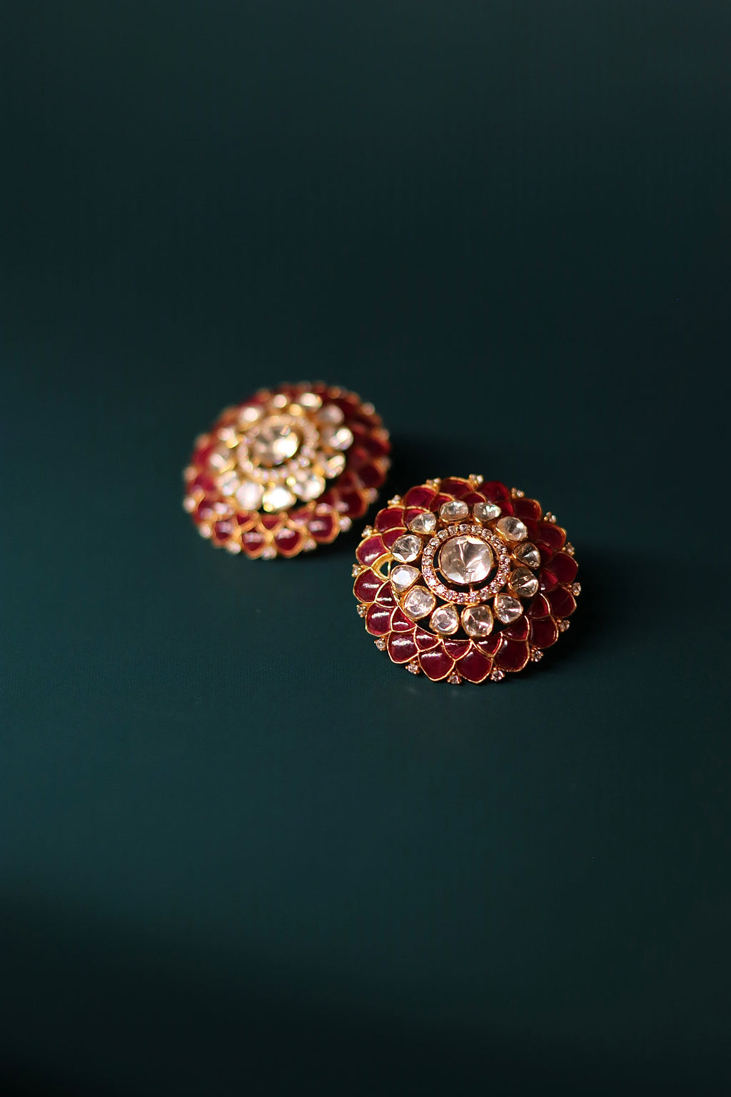 Sia Polki Gulaal Studs – domed ruby red and moissanite polki stud earrings with concentric petal layers, handcrafted in Jodhpur, photographed on teal background