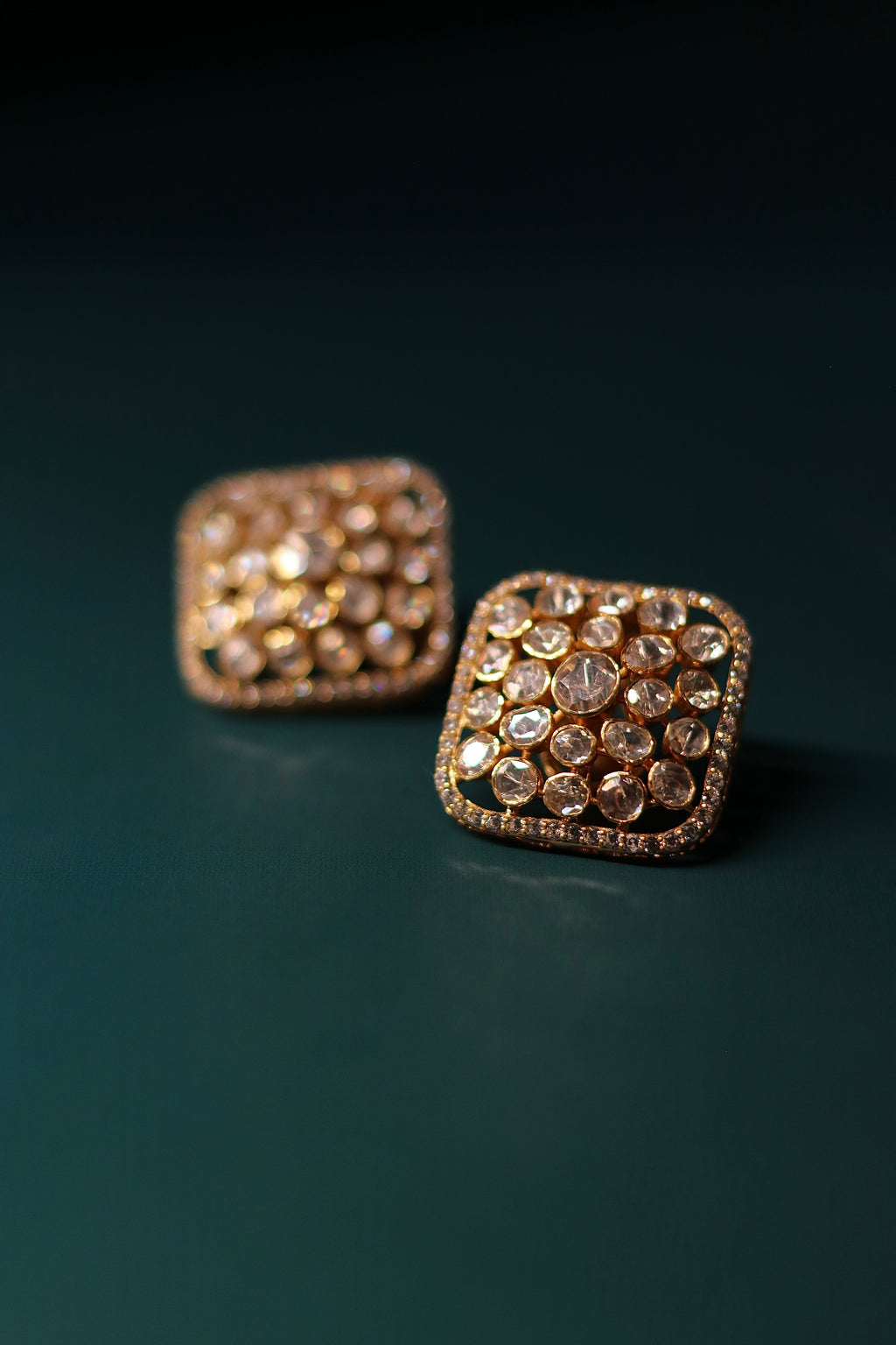 Sia Polki Choras Studs – cushion-shaped moissanite polki stud earrings fully paved in polki with AD stone border, handcrafted in Jodhpur, photographed on teal background